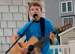 Ethan Bayer playing guitar and singing at an outdoor performance.